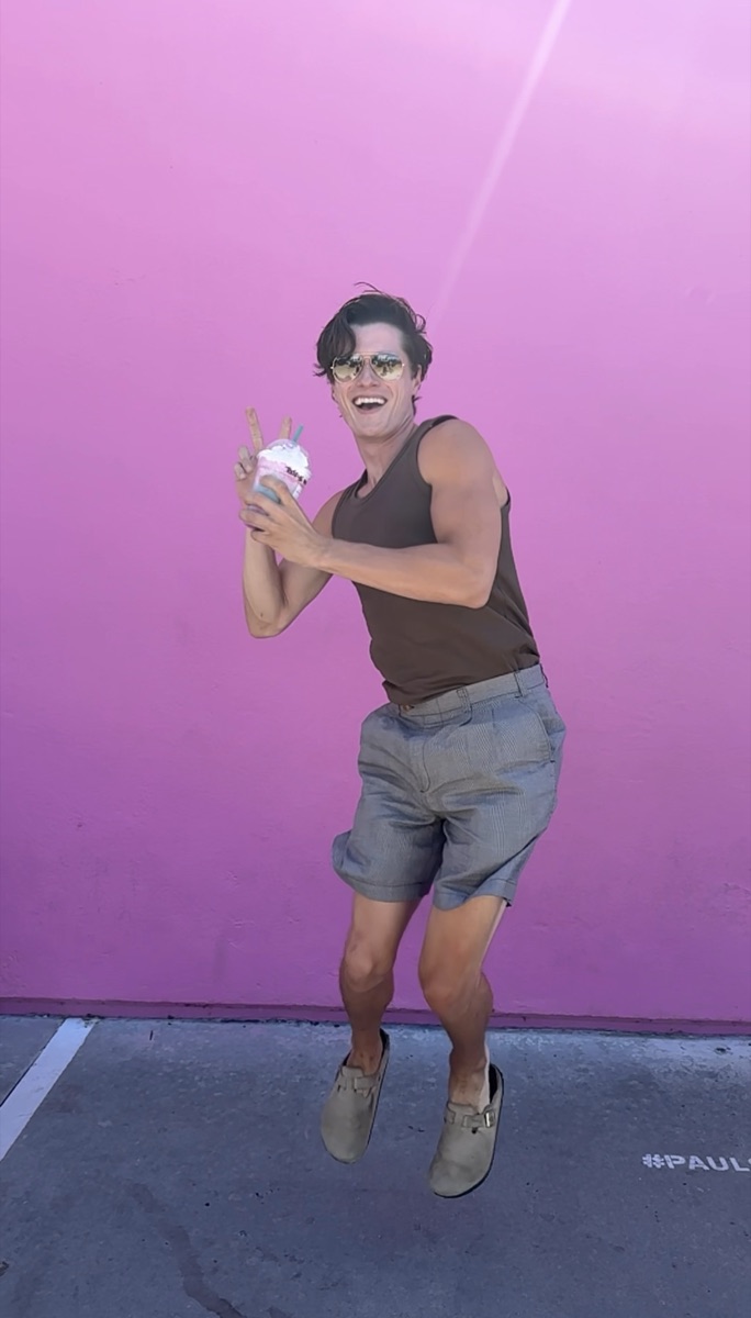 Doug mid-jump in front of a pink wall, ice cream in hand